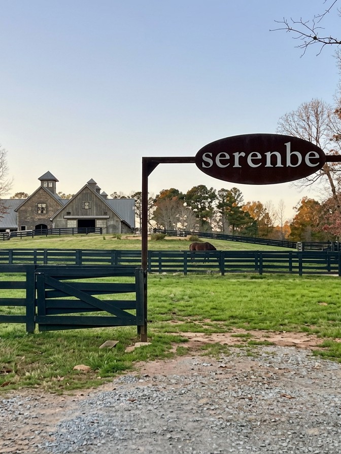 The entrance to Serenbe, its sign above a gravel drive with the community's farm buildings beyond